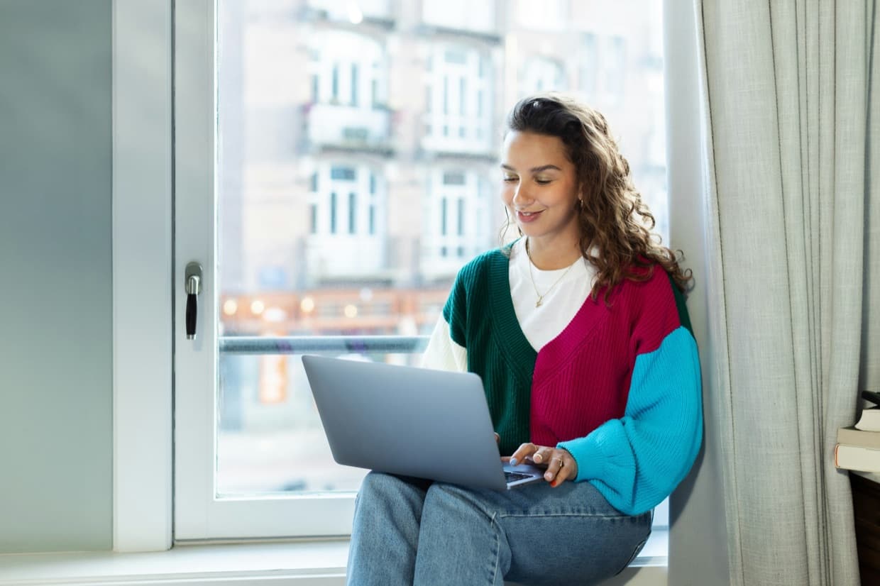 A freelancer working on a laptop by a window